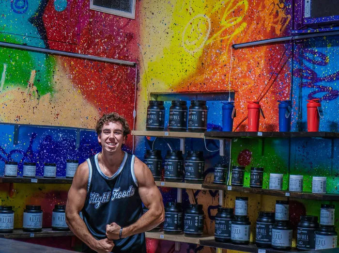 Thomas Lahart, founder of Flight Foods, flexing in front of a wall of Flight Foods tubs